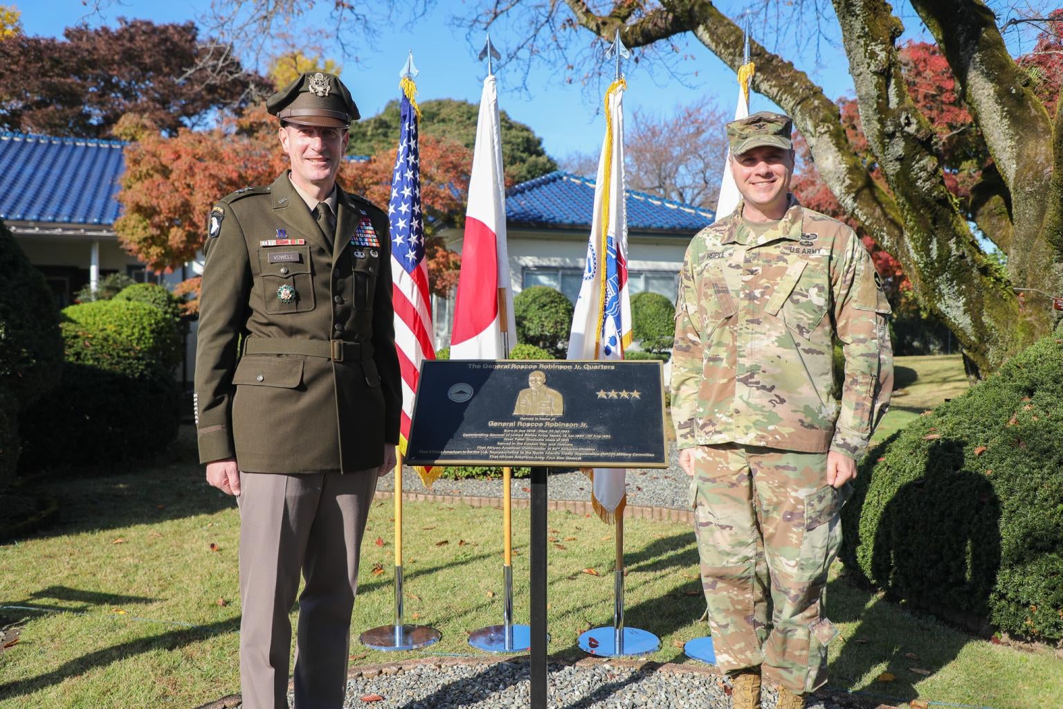 "Major General Joel “JB” Vowell, Commander of U.S. Army Japan (left) and Colonel Geoffrey Heiple, Director of Army Reserve Affairs (right), at the dedication of Quarters 1000 as The General Roscoe Robinson Jr Quarters in Japan. The two men stand outside Quarters 1000 in army uniforms around a placard with information about Roscoe Robinson."