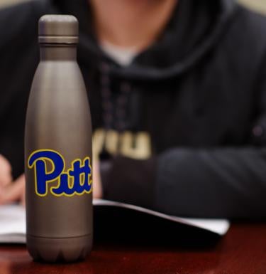 Undergraduate student sits at desk with Pitt water bottle 