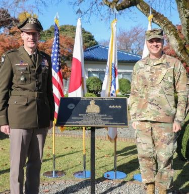 "Major General Joel “JB” Vowell, Commander of U.S. Army Japan (left) and Colonel Geoffrey Heiple, Director of Army Reserve Affairs (right), at the dedication of Quarters 1000 as The General Roscoe Robinson Jr Quarters in Japan. The two men stand outside Quarters 1000 in army uniforms around a placard with information about Roscoe Robinson."